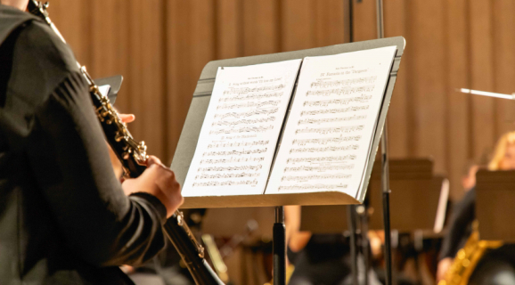 Músico a tocar clarinete em palco, lendo uma partitura num suporte, durante um ensaio ou concerto de orquestra