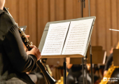 Músico a tocar clarinete em palco, lendo uma partitura num suporte, durante um ensaio ou concerto de orquestra