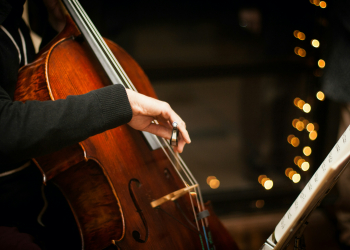 Pessoa a tocar violoncelo ao lado de uma pauta musical, com luzes decorativas ao fundo
