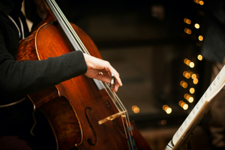 Pessoa a tocar violoncelo ao lado de uma pauta musical, com luzes decorativas ao fundo